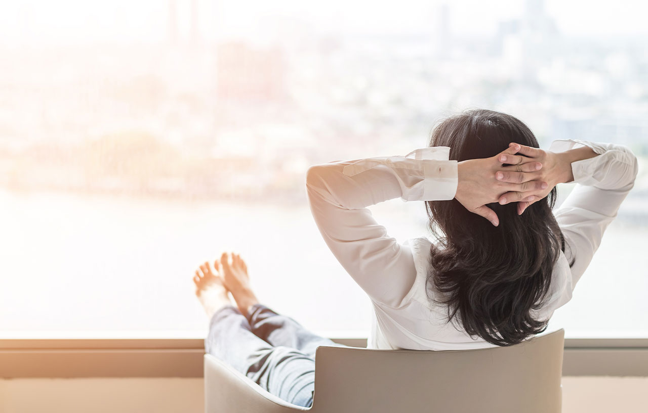 Business woman relaxing with her feet up and hands behind her head looking out of a hotel window