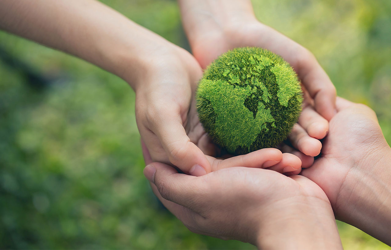 A grass-shaped planet earth cupped in two pair of hands